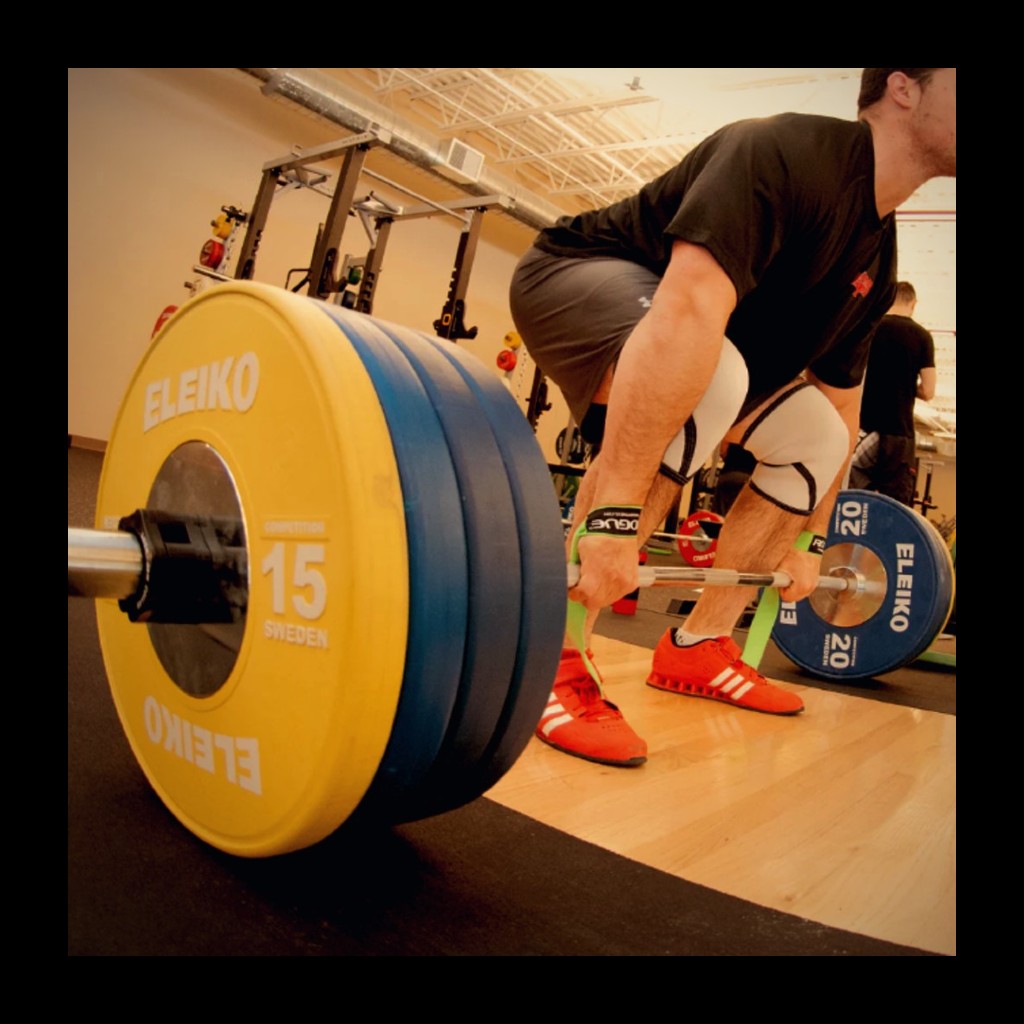 a male weightlifter performing a deadlift on an olympic platform wearing weightlifting shoes