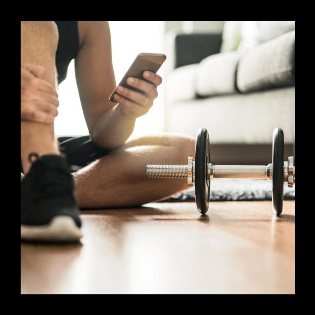 man sitting on the floor inside using his mobile phone next to a dumbbell