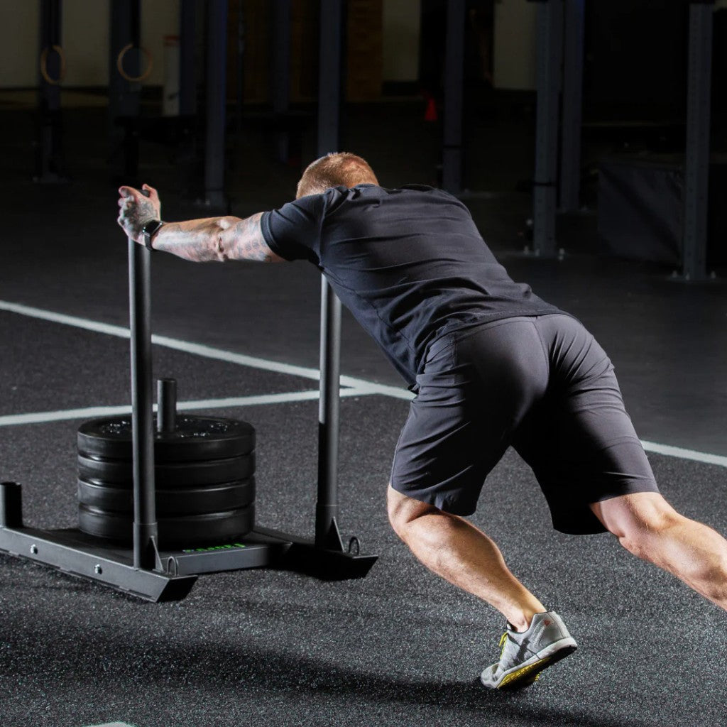 a strong male fitness athlete pushing a weighted sled on an astro turf track.