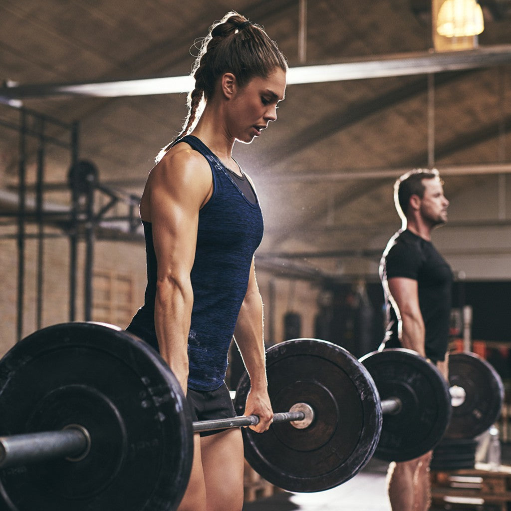 a strong looking female athlete deadlifting a barbell off the ground with a ponytail.