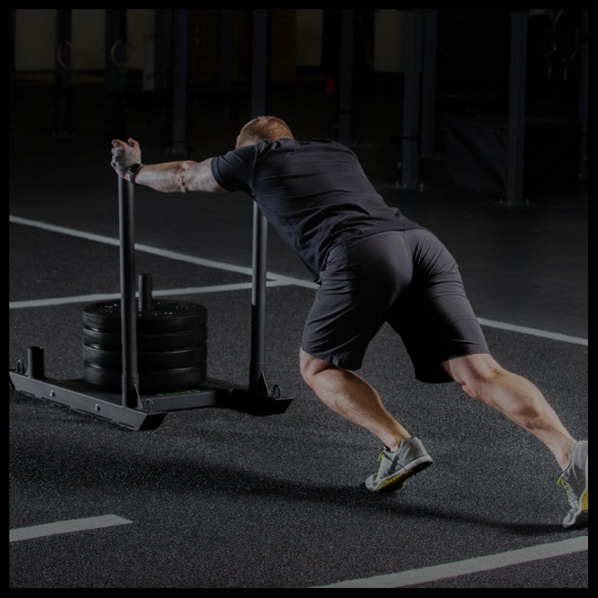 a fitness athlete pushing a sled with weight on it over astro turf