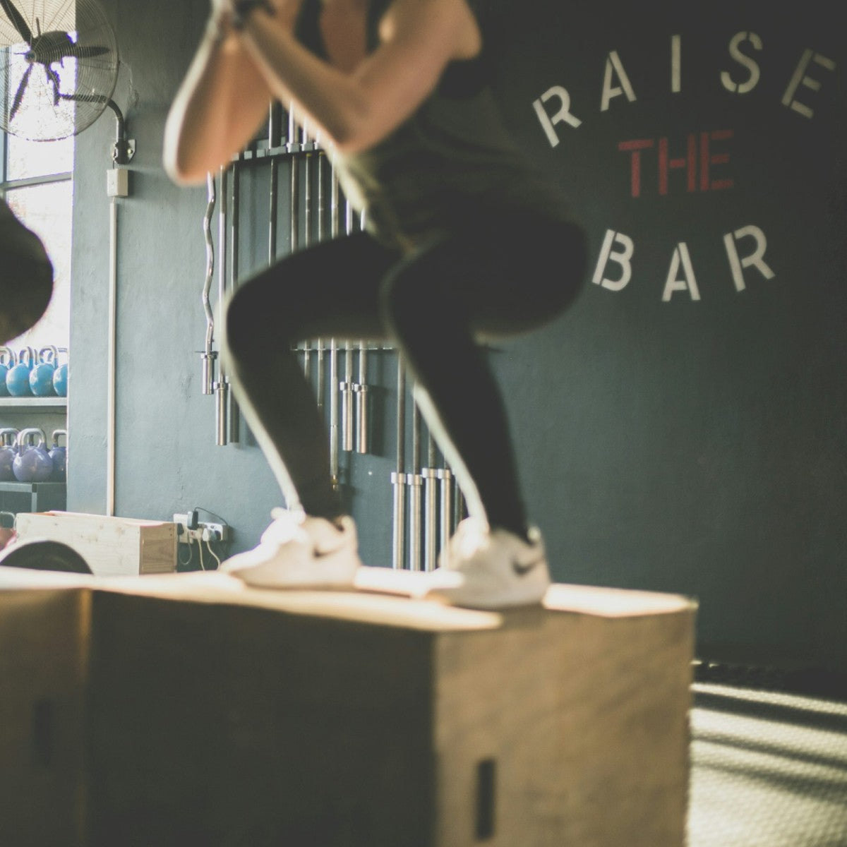 woman jumping on box during a fitness class with the words raise the bar behind her on the wall.
