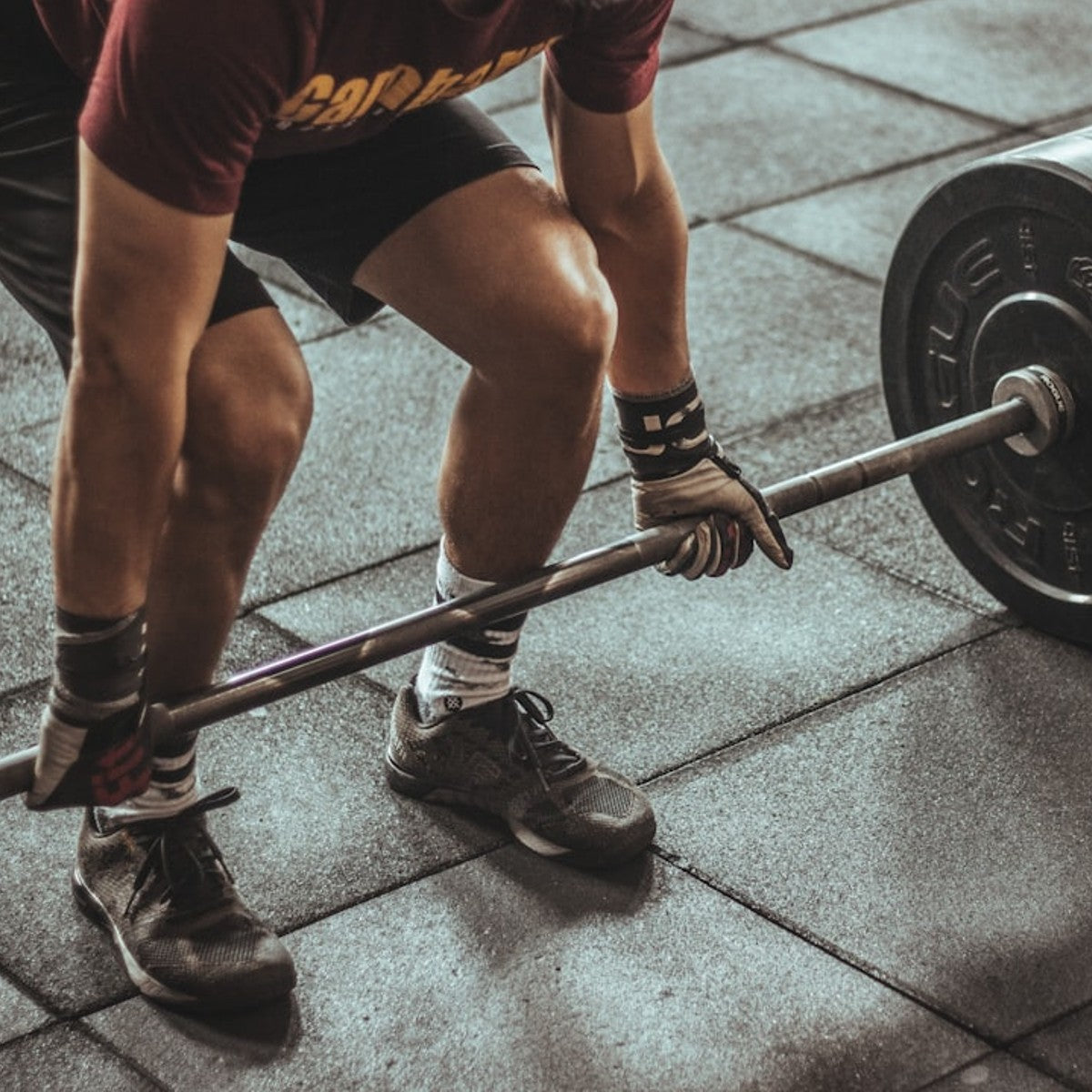 a male gym member deadlifting a barbell off the floor wearing gym gloves.