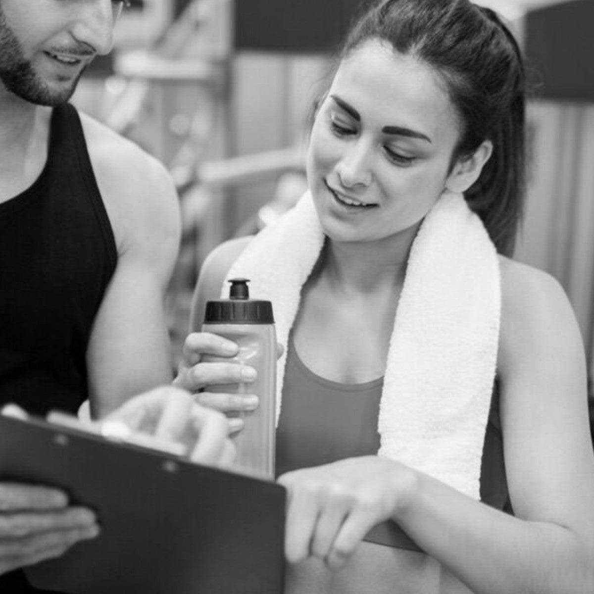 a personal trainer showing a gym client a checklist board at the end of a training session.